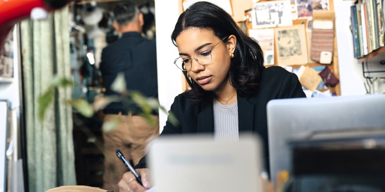 Woman with a laptop making notes on paper