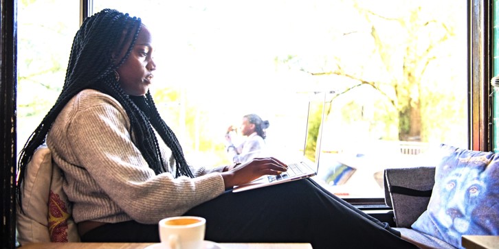 Woman working from home with a laptop on her lap an coffee nearby